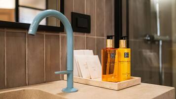 Un baño con un grifo azul, un mueble de tocador de madera y dos botellas de loción corporal y para manos sobre la encimera.
