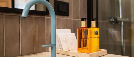 A bathroom with a blue faucet, a wooden vanity, and two bottles of hand and body lotion on the counter.