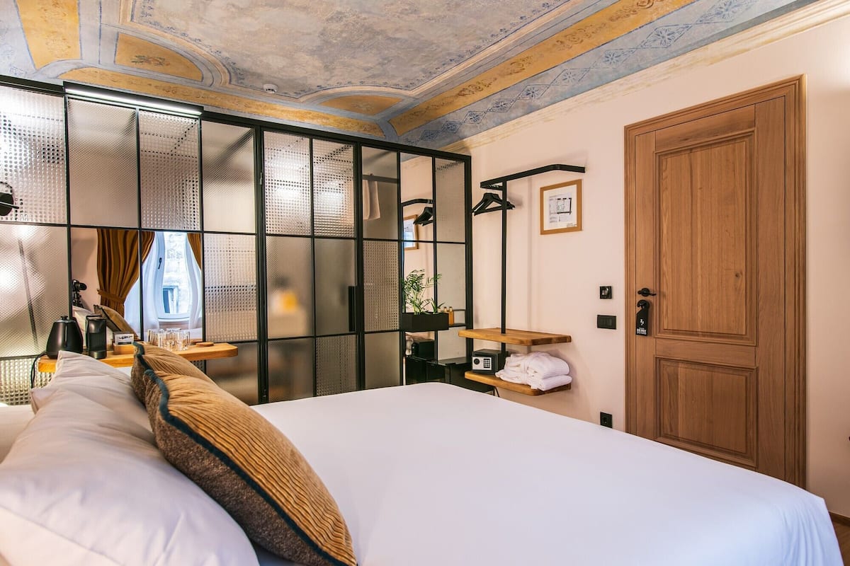 Habitación de hotel con cama, armario de madera, espejo, repisa con artículos de aseo y techo decorativo.