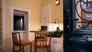 Habitació compacta amb escriptori, dues cadires, un ordinador portàtil, una planta en test i una porta amb una aldreta decorativa.