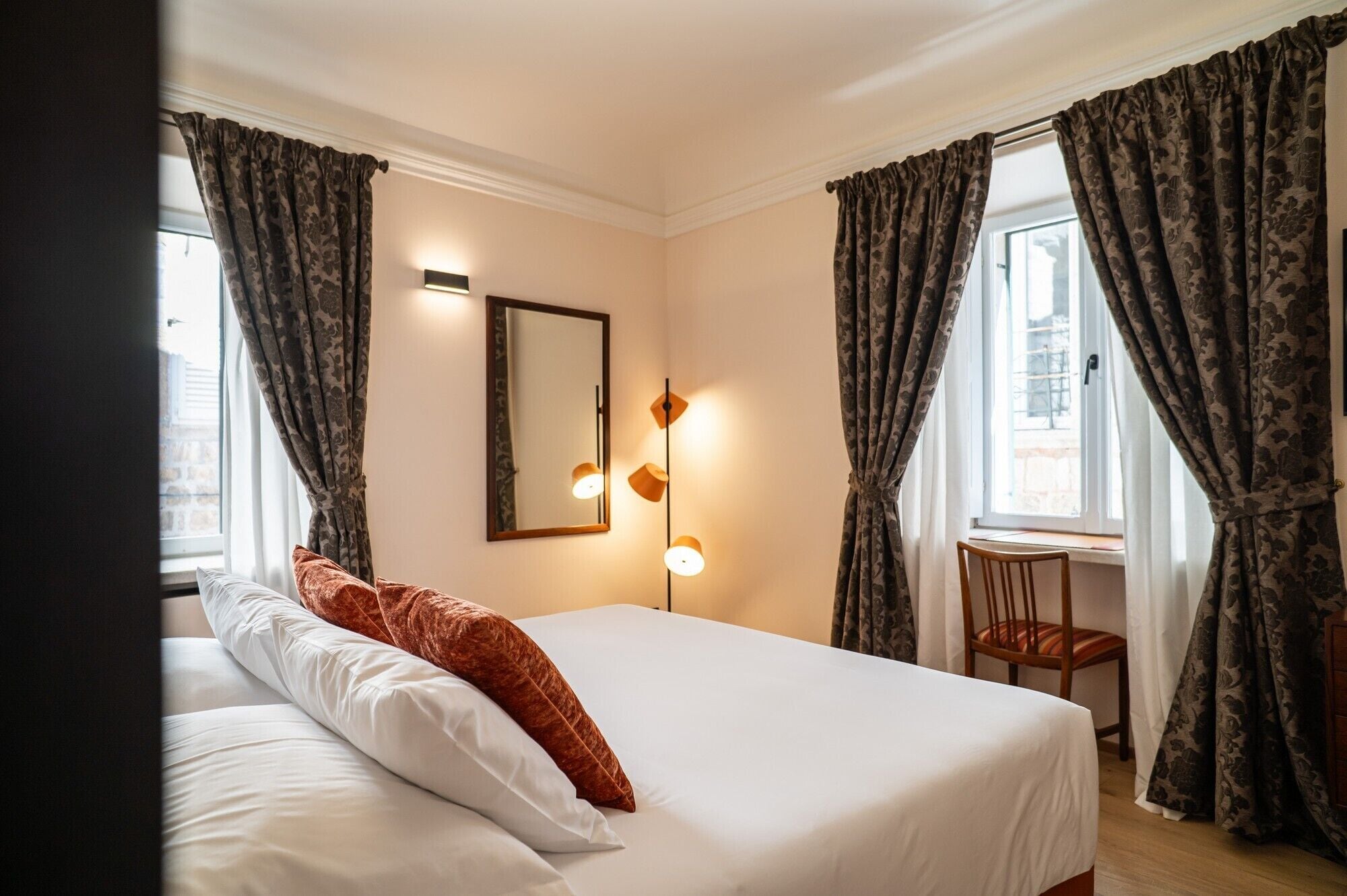 Ein Hotelzimmer mit Bett, Stuhl, Schreibtisch und einem Fenster mit Vorhängen.
