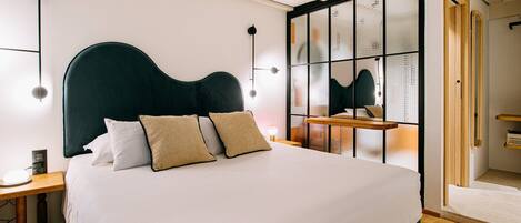 A modern bedroom with a large bed, a wooden nightstand, a bedside table, and a large mirror.