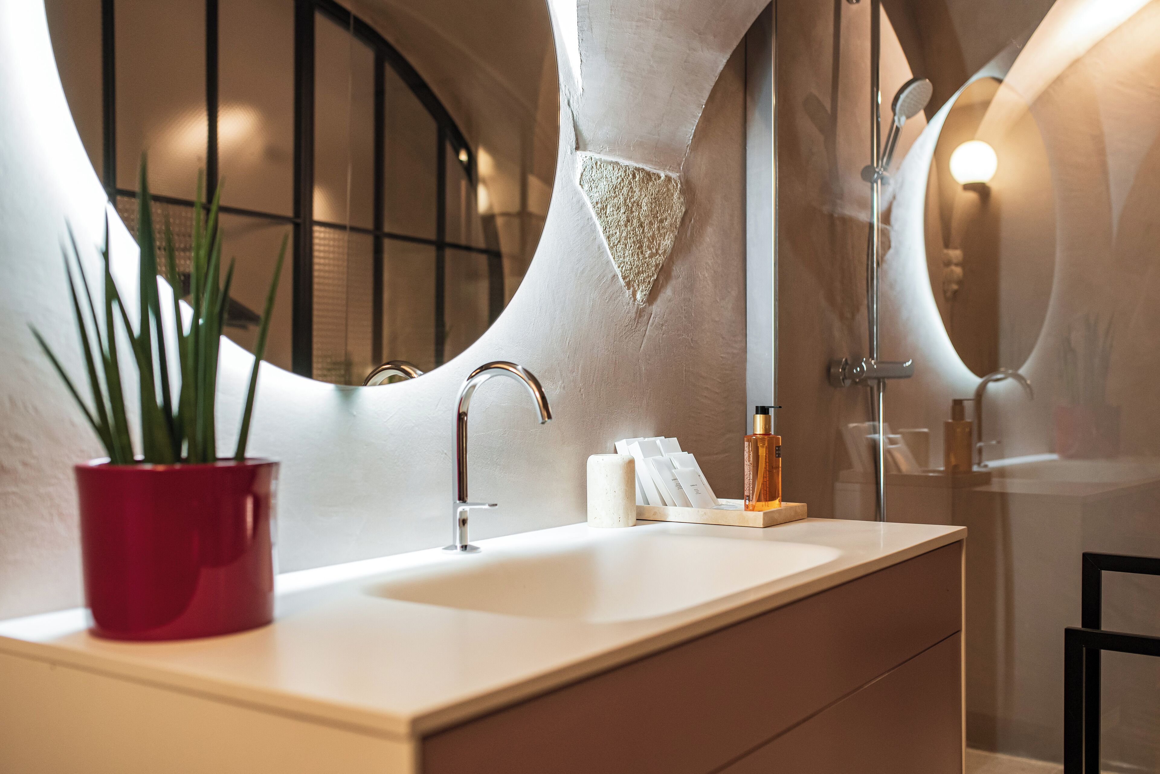 Ein modernes Badezimmer mit einem weißen Waschbecken, einem roten Blumentopf, einem Spiegel und einer Duschkabine.