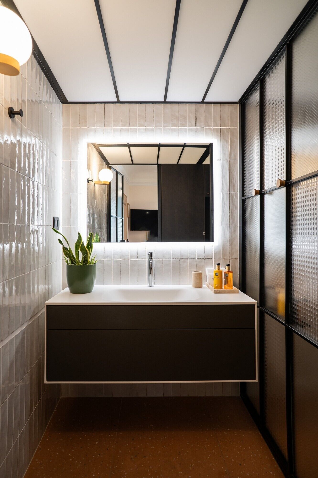 Un bagno moderno con un grande specchio, un lavandino bianco e una pianta in vaso.