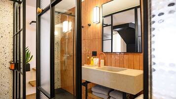 Une salle de bain moderne avec une douche à parois de verre, un lambris en bois, un grand miroir et un plan de toilette avec des articles de toilette.