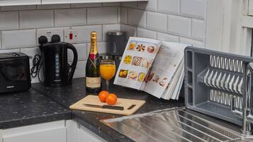 A kitchen counter with a coffee maker, a bottle of champagne, a glass of orange juice, a cutting board with a knife, and a magazine.