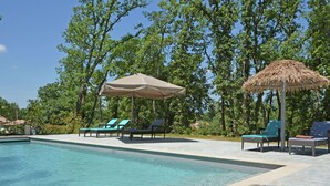 A swimming pool with lounge chairs and umbrellas. - Villa in Montauroux with Pool and Forest Views (Montauroux)
