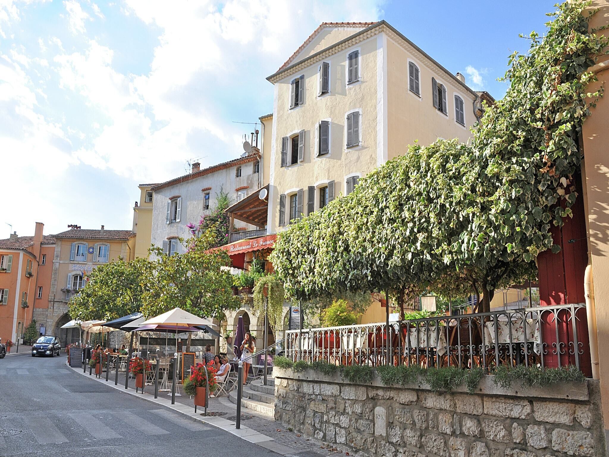 Une rue bordée de terrasses, avec des murs en pierre et des bâtiments dotés de balcons.