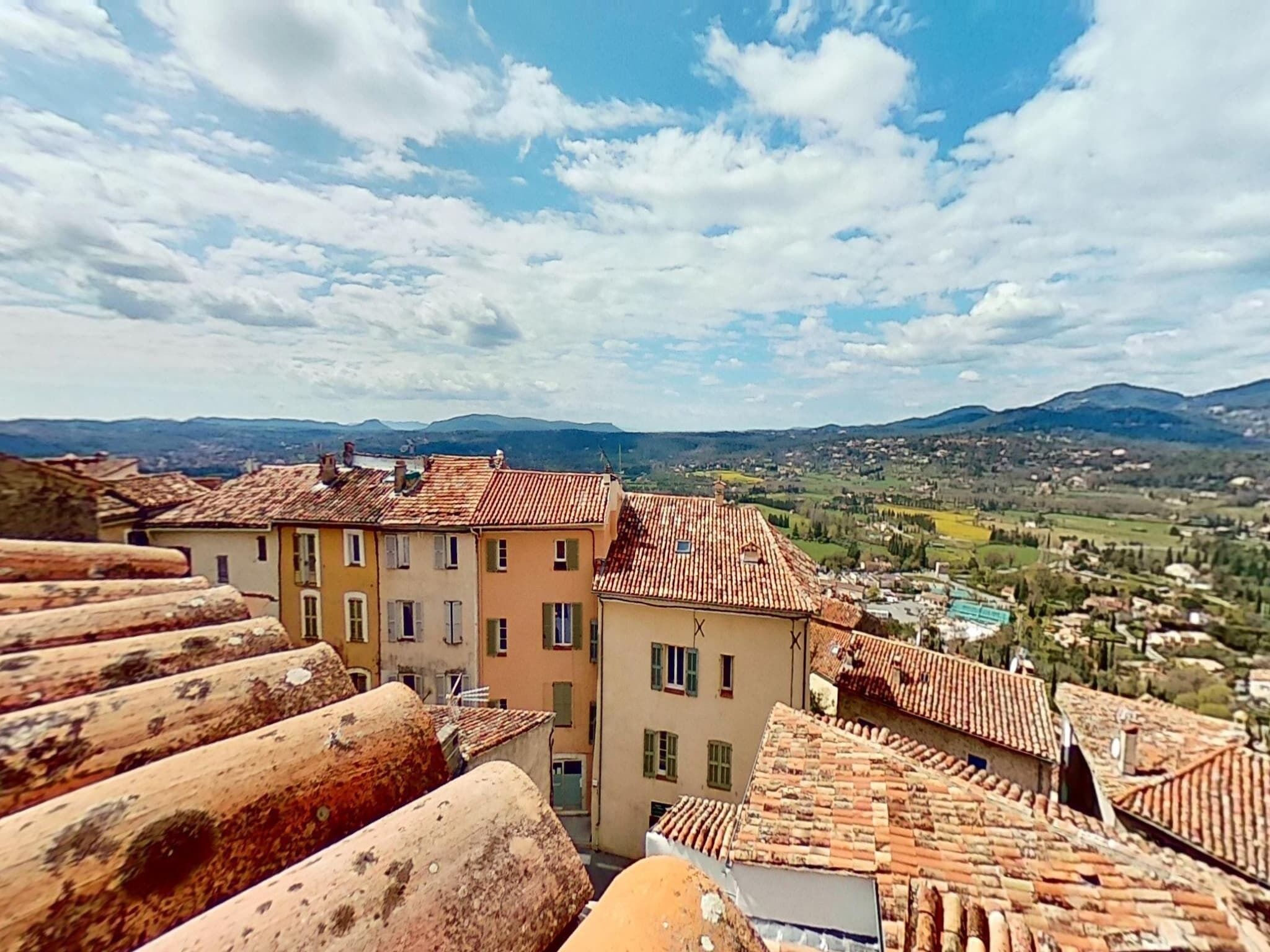 A view of terracotta-roofed buildings with a valley and mountains in the background.