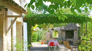Un patio rústico al aire libre con paredes de piedra, una mesa con sillas y una lámpara colgante.