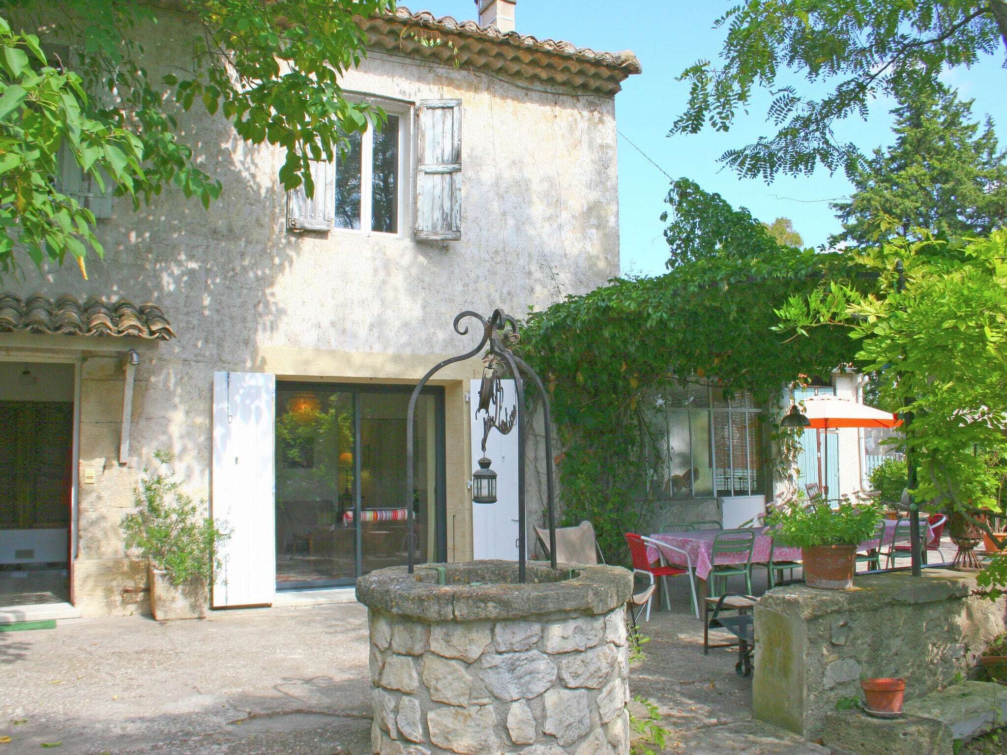 A rustic stone building with a tiled roof, a stone well, and outdoor seating with tables and chairs.