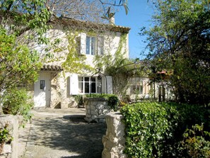 A stone building with a rustic charm, featuring a stone staircase leading to a wooden door, surrounded by lush greenery and a clear blue sky. - Holiday Home in Provence with Private Pool (Cavaillon)