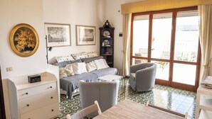 Una habitación con cama, escritorio, silla, mesa, estantería y un amplio ventanal.