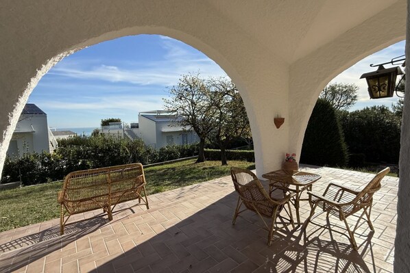 A covered patio with wicker furniture, a table, and a bench.