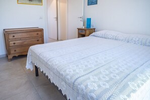A bedroom with a bed, a wooden dresser, a nightstand, and a door.