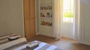 Ein Schlafzimmer mit Bett, Kleiderschrank, Bücherregal und einem Fenster mit Vorhängen.