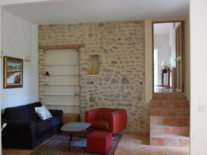 A living room with a stone wall, a red sofa, a blue sofa, a small table, and a framed picture on the wall. - Villa in Valréas with Pool and Garden Views (Valréas)