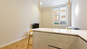 A modern kitchen with a white countertop, wooden floor, and a window with a view of buildings.