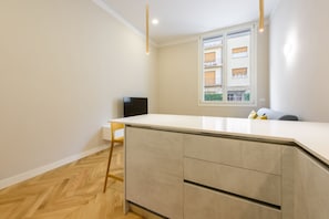 A modern kitchen with a white countertop, wooden floor, and a window with a view of buildings.