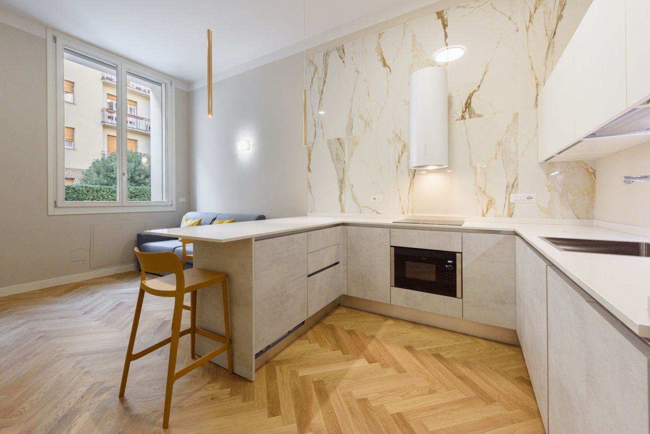 Eine moderne Küche mit Marmorfliesenspiegel, integriertem Backofen und einem großen Fenster.