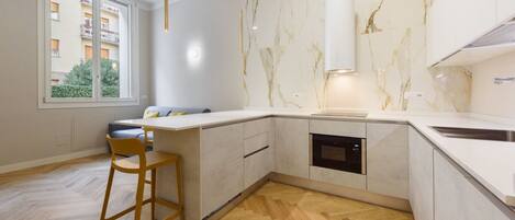 A modern kitchen with a marble backsplash, built-in oven, and a large window.