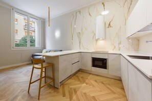 A modern kitchen with a marble backsplash, built-in oven, and a large window.