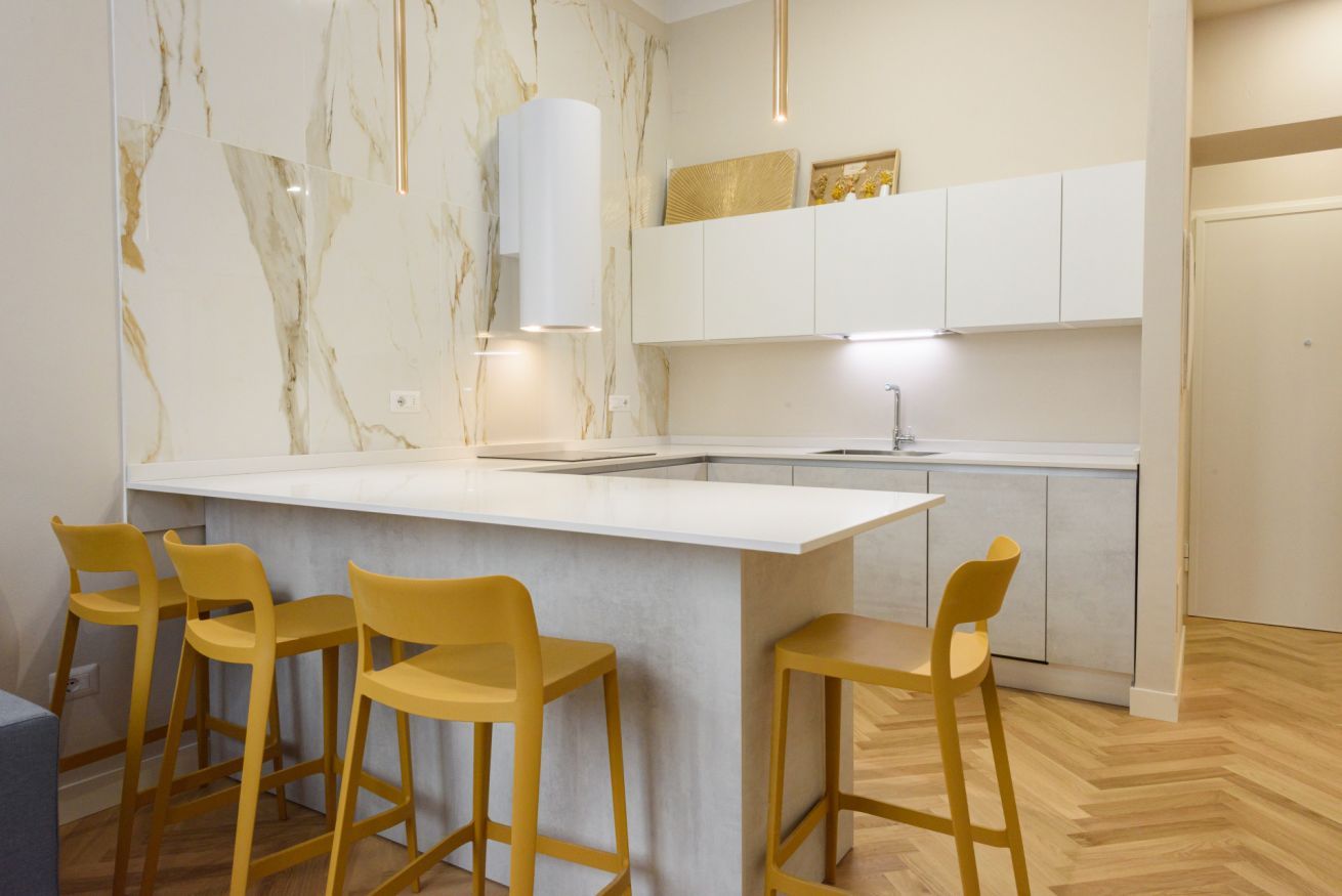 Una cucina moderna con schienale in marmo, mobili bianchi e un'isola centrale con sgabelli da bar.