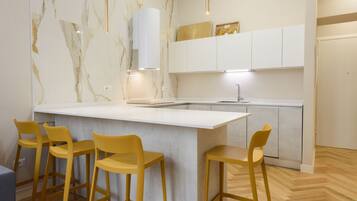 Una cucina moderna con schienale in marmo, mobili bianchi e un'isola centrale con sgabelli da bar.