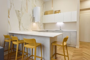 A modern kitchen with a marble backsplash, white cabinetry, and a central island with bar stools.