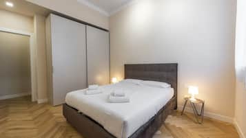 Camera da letto con un ampio letto, un armadio, un comodino con una lampada e un pavimento in legno con motivo a spina di pesce.