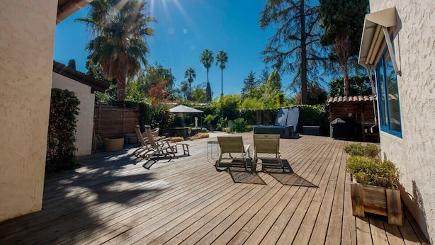 A wooden deck with lounge chairs and a table, surrounded by greenery and trees. - 06V - Beautiful villa with spa, pool and tennis (Biot)