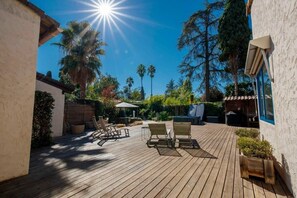 A wooden deck with lounge chairs and a table, surrounded by greenery and trees. - 06V - Beautiful villa with spa, pool and tennis (Biot)