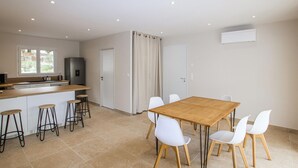 Una cocina moderna con refrigerador integrado, una ventana y una zona de comedor con mesa de madera y sillas blancas.