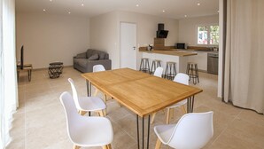 Una cocina moderna con una isla central, una zona de comedor con una mesa de madera y sillas blancas, y un sofá gris en una amplia sala de estar.