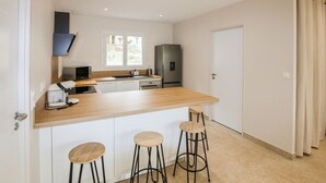 Una cocina moderna con mostrador de madera, microondas integrado, refrigerador y tres taburetes de bar.