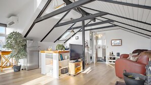 A spacious loft with high ceilings, exposed beams, a wooden floor, a modern kitchen, a living area with a red leather sofa, and a television. - Lovely home in Hadsund with WiFi (Hadsund)