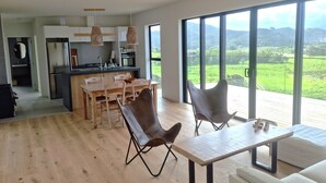 A modern kitchen with a dining area, large windows with a view of the countryside, and a cozy seating area with a sofa and chairs.