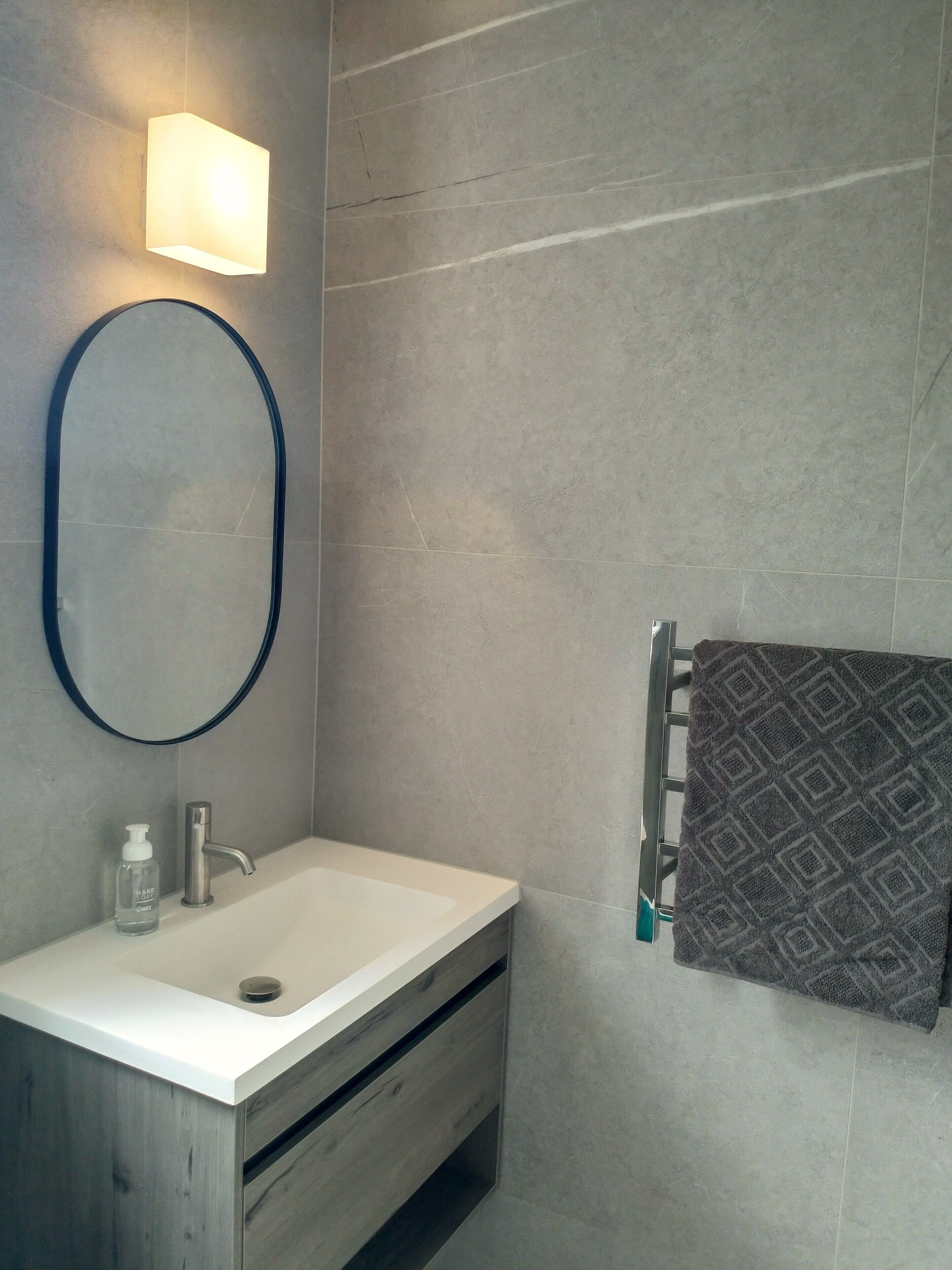 A bathroom with a white sink, a mirror, a towel rack with a patterned towel, and a wall-mounted light.