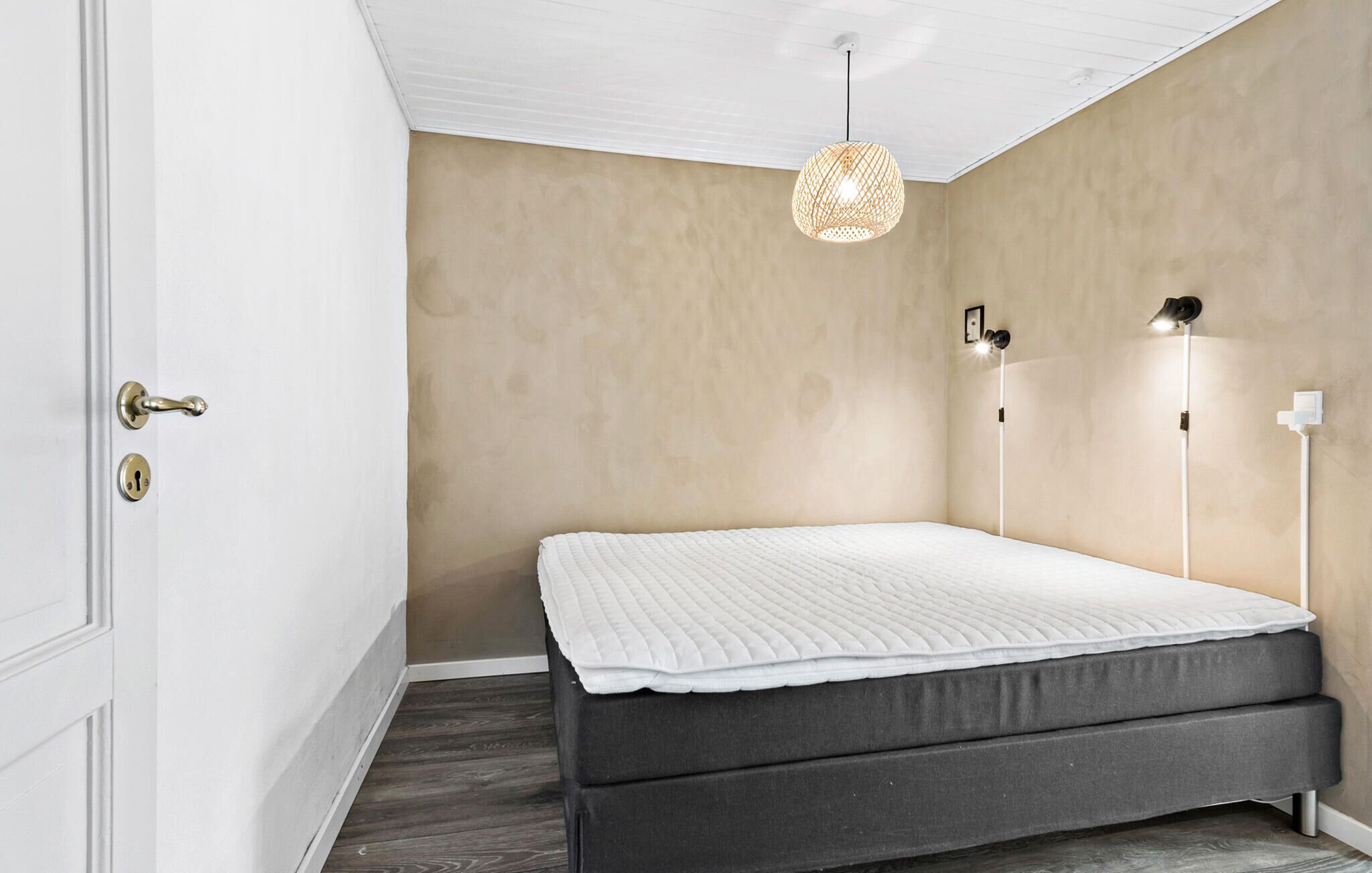 A bedroom with a bed, a door, a light fixture, and a wall.
