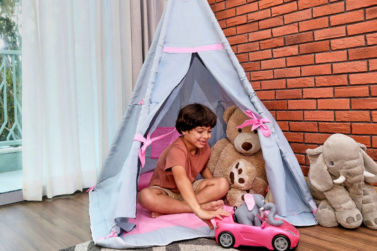 Un niño jugando dentro de una carpa con peluches y un coche de juguete.
