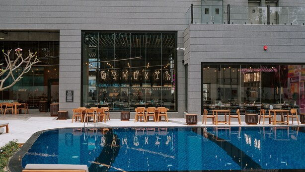 Un bâtiment moderne doté d’une piscine, d’un espace extérieur aménagé et d’un restaurant avec de grandes fenêtres.
