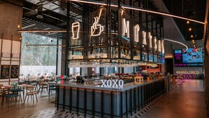 Un espace bar moderne agrémenté d’un néon affichant le message « XOXO » et d’un grand écran diffusant les mots « Let’s Play Tag » et le hashtag « #BANGLORE’D ».