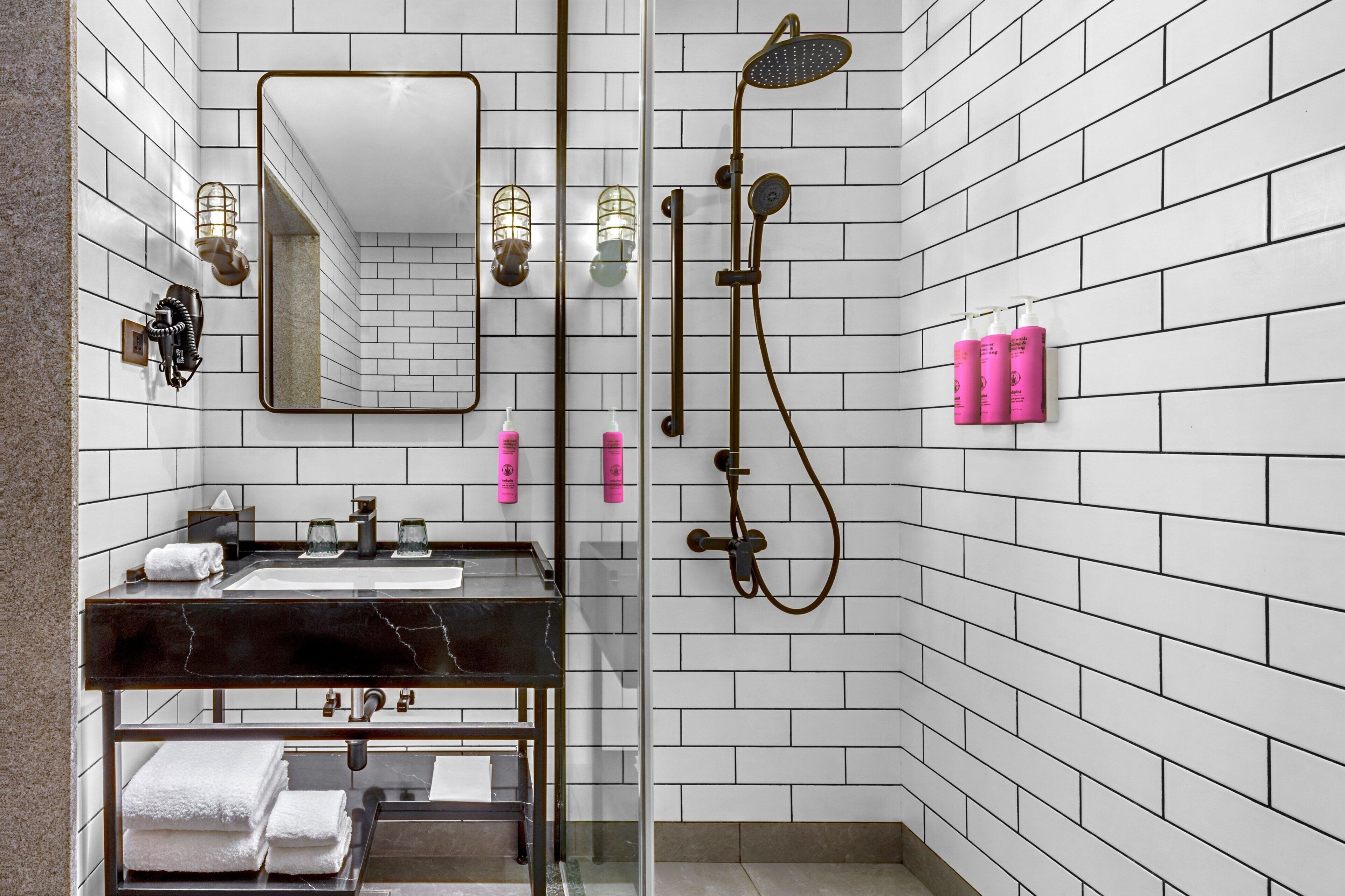 A modern bathroom with a marble sink, a glass shower enclosure, and white tiled walls.