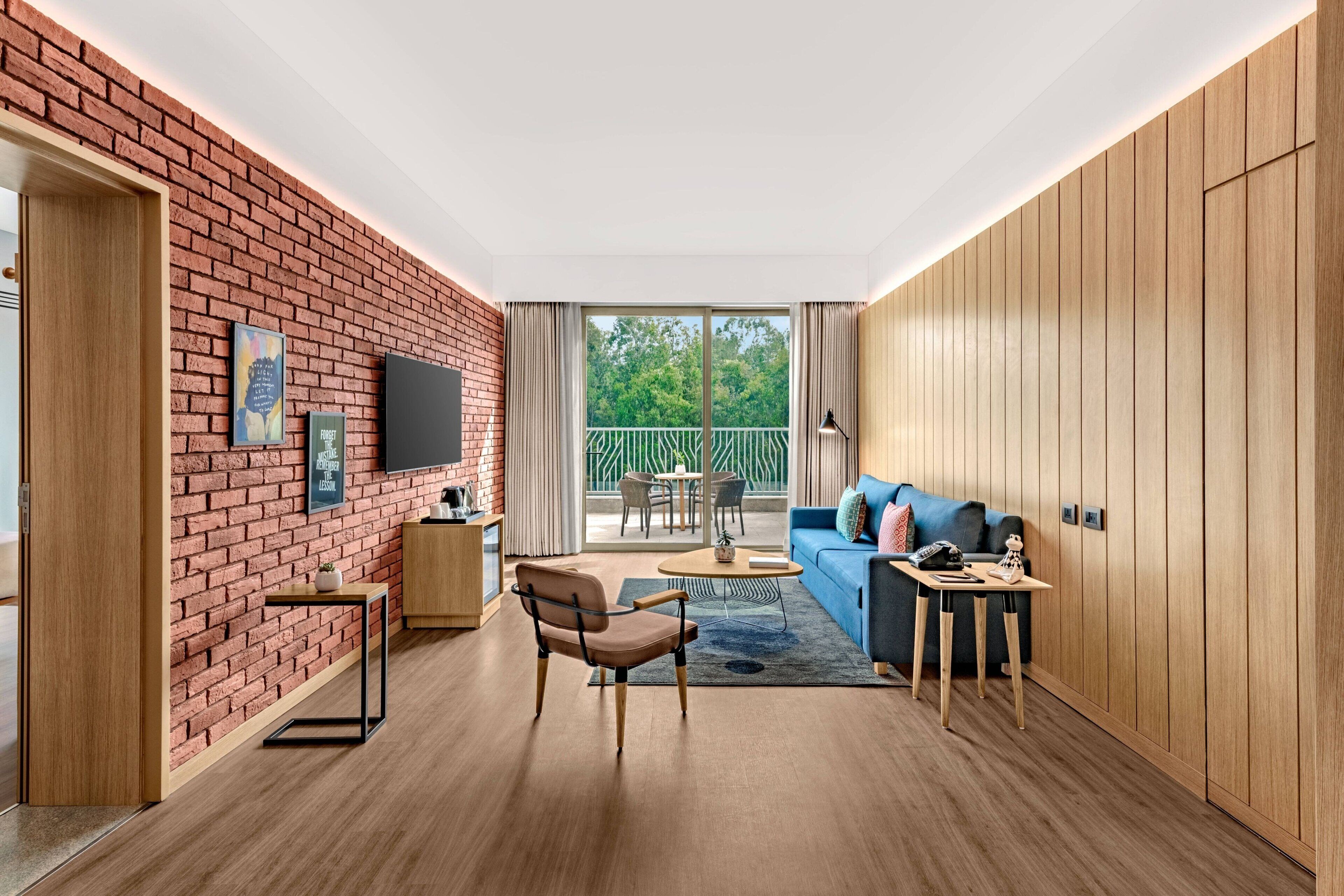 A modern living room with a brick wall, wooden paneling, a blue sofa, a coffee table, and a TV mounted on the wall.