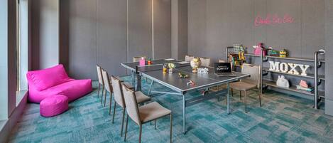 A modern meeting room with a large table, chairs, a pink sofa, and a bookshelf with toys and a globe.