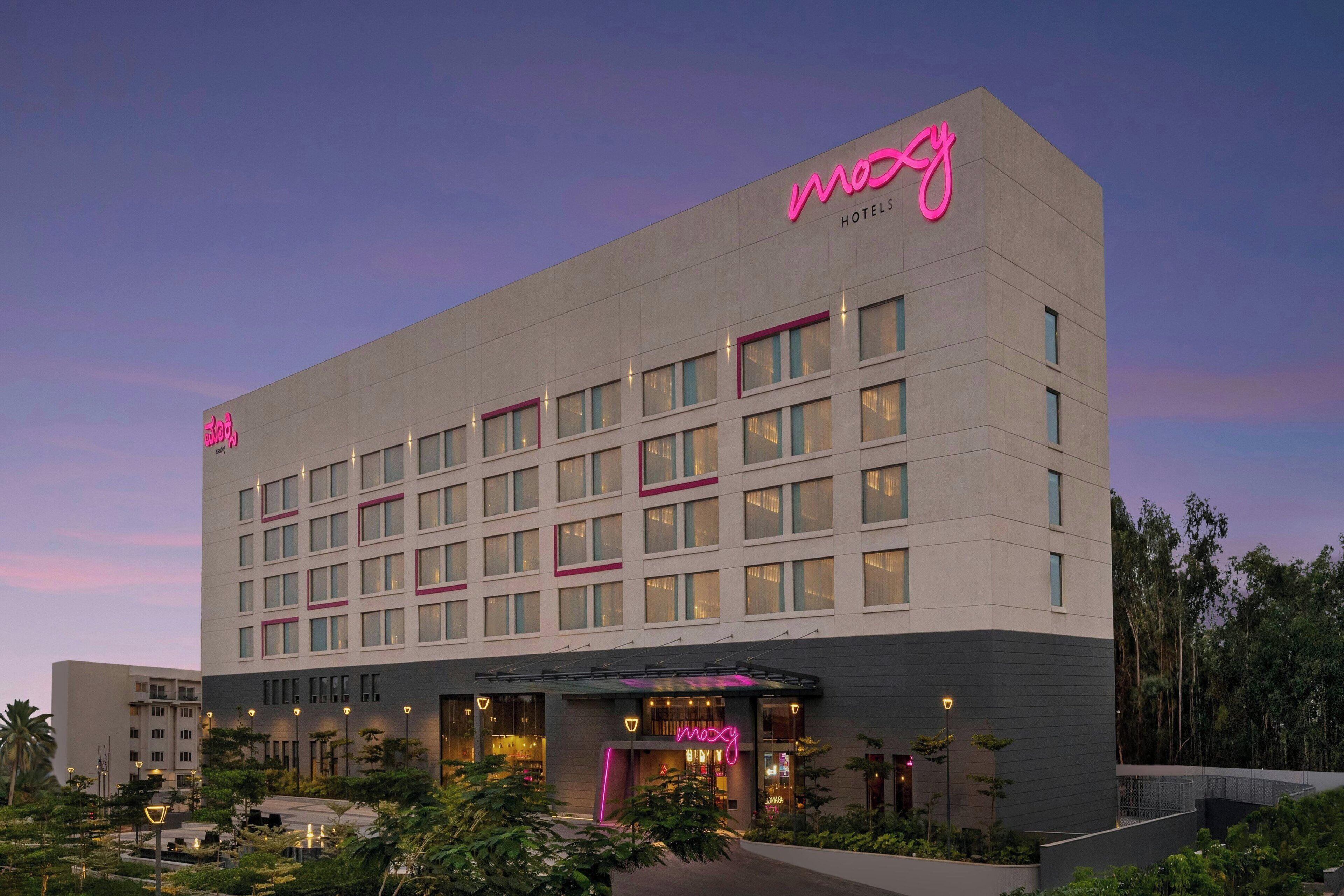 A modern hotel building with a prominent 'mozy' sign, multiple floors, and a well-lit entrance.