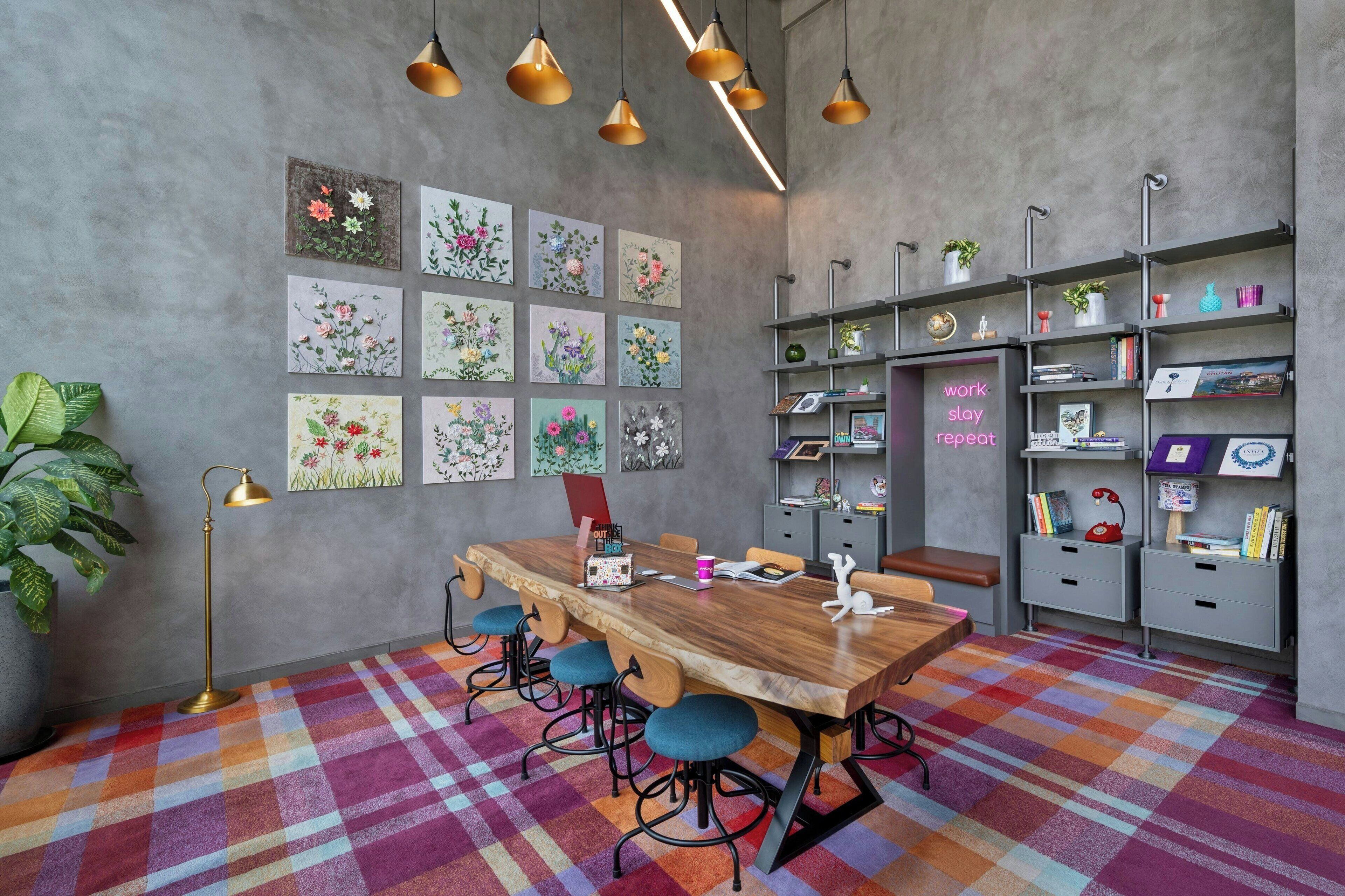 A modern meeting room with a wooden table, blue chairs, a colorful plaid carpet, and a wall decorated with floral artwork.