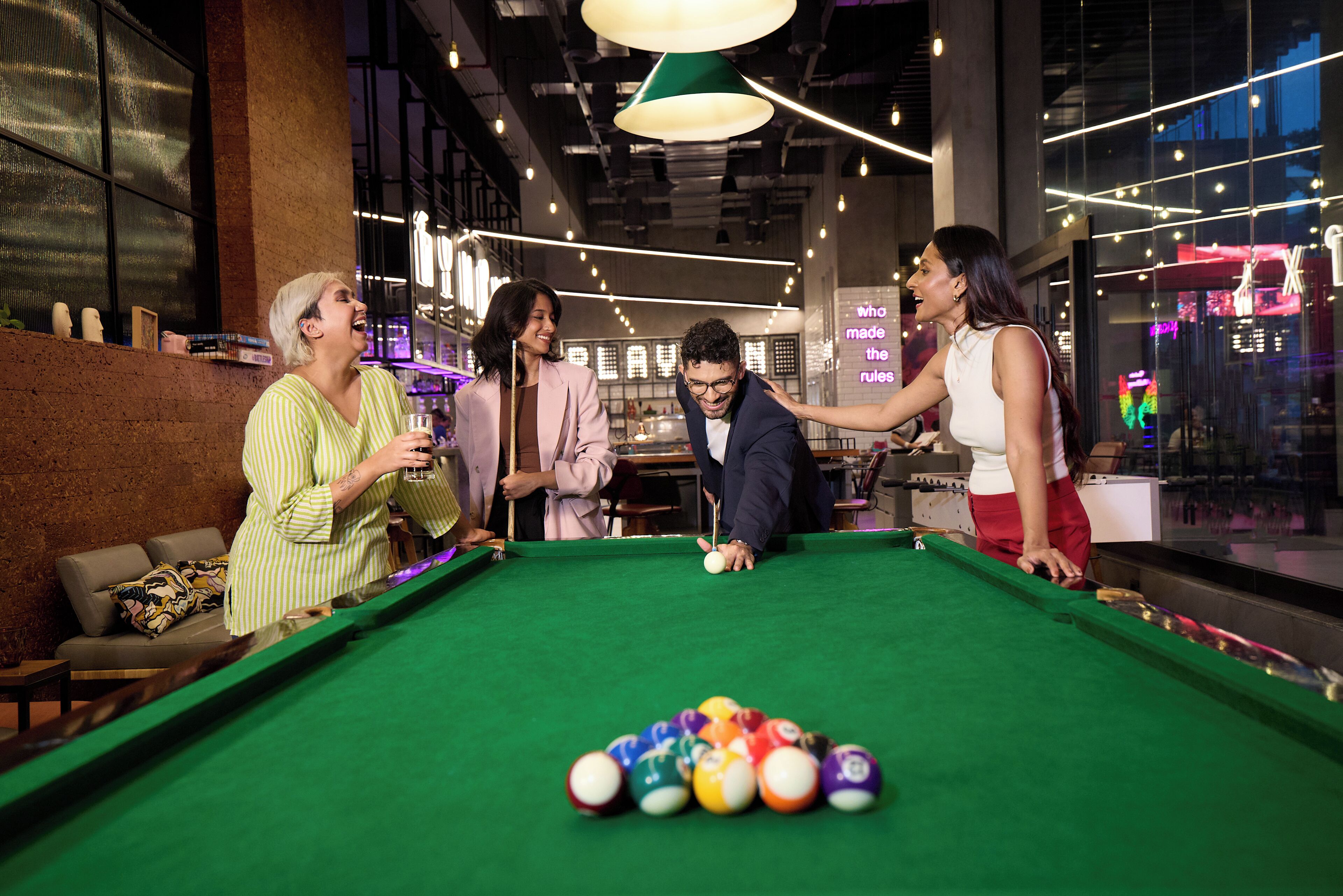 Une table de billard avec des billes, un canapé et un coin bar avec des bouteilles.