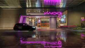 Un bâtiment moderne avec une enseigne au néon sur laquelle on peut lire « mozy », et une voiture garée devant.
