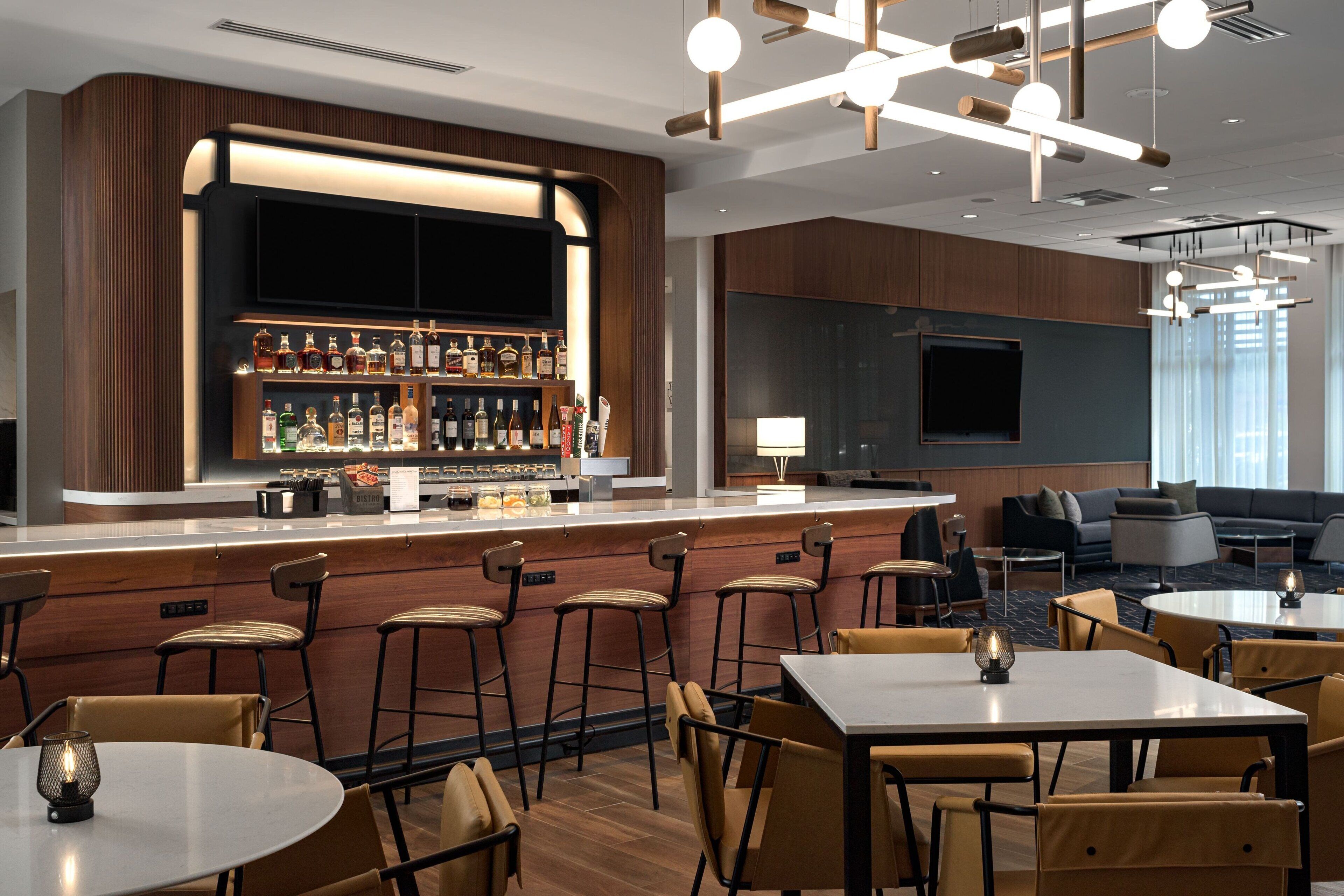 A bar area with stools, a TV, and a variety of bottles. There are tables and chairs for dining.